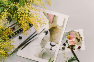 A watercolor painting of a bunny surrounded by mimosa flowers and art supplies.